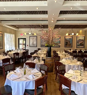 Elegant dining room of Sergio's de Pelham with white tablecloths and framed vintage Italian travel posters by Alecse displayed on the walls.