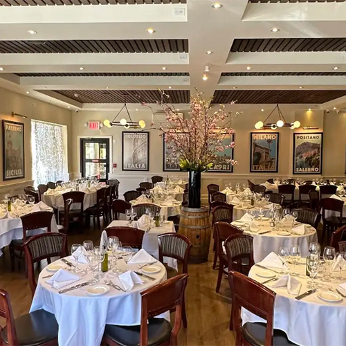 Elegant dining room of Sergio's de Pelham with white tablecloths and framed vintage Italian travel posters by Alecse displayed on the walls.