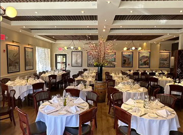 Elegant dining room of Sergio's de Pelham with white tablecloths and framed vintage Italian travel posters by Alecse displayed on the walls.