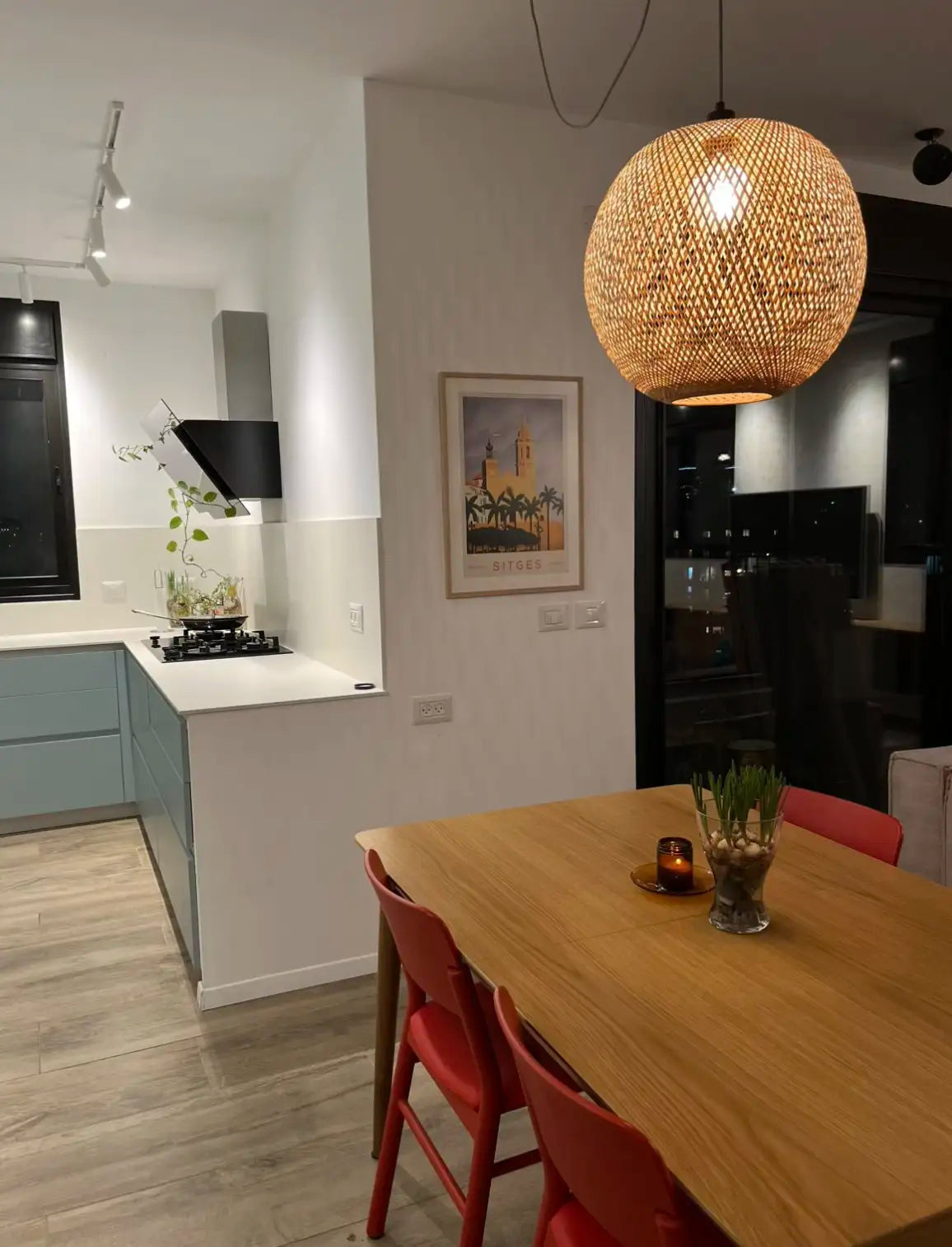 Minimalist dining room with red chairs, warm pendant light and the framed Sitges Sunset poster by Cha hanging on the wall, creating a balanced and elegant interior composition.