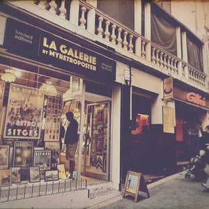 View of La Galerie by Myretroposter in Sitges with people lining up for waffles at the Gofras stand next door – the real-life inspiration behind the Sitges Waffles Poster by Cha. Limited edition food art print.