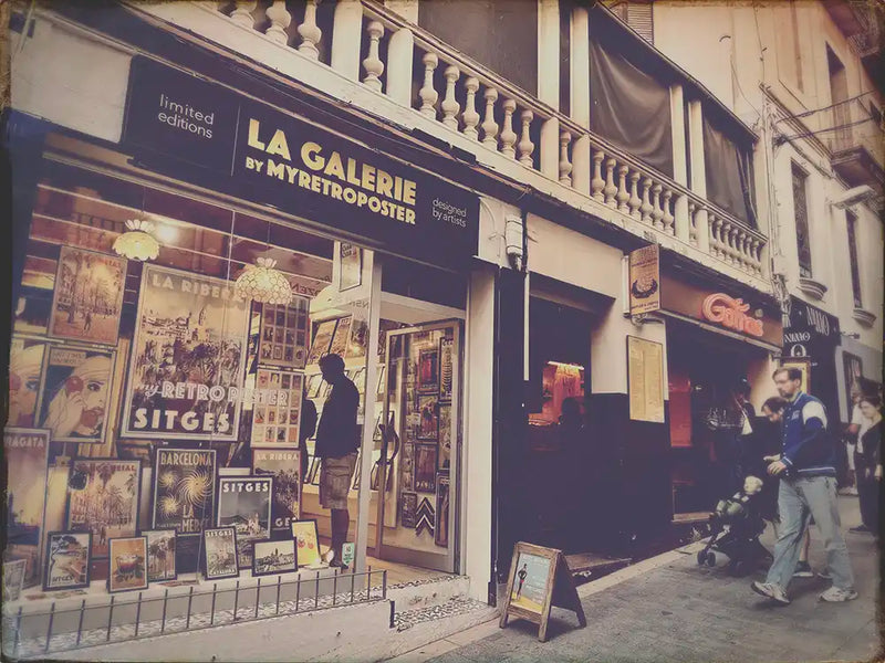 View of La Galerie by Myretroposter in Sitges with people lining up for waffles at the Gofras stand next door – the real-life inspiration behind the Sitges Waffles Poster by Cha. Limited edition food art print.