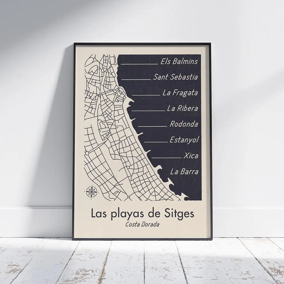 Framed Las Playas de Sitges map poster by Cha from The Wanderer Maps x Spanish Capsule collection displayed against a wall on a white wooden floor.