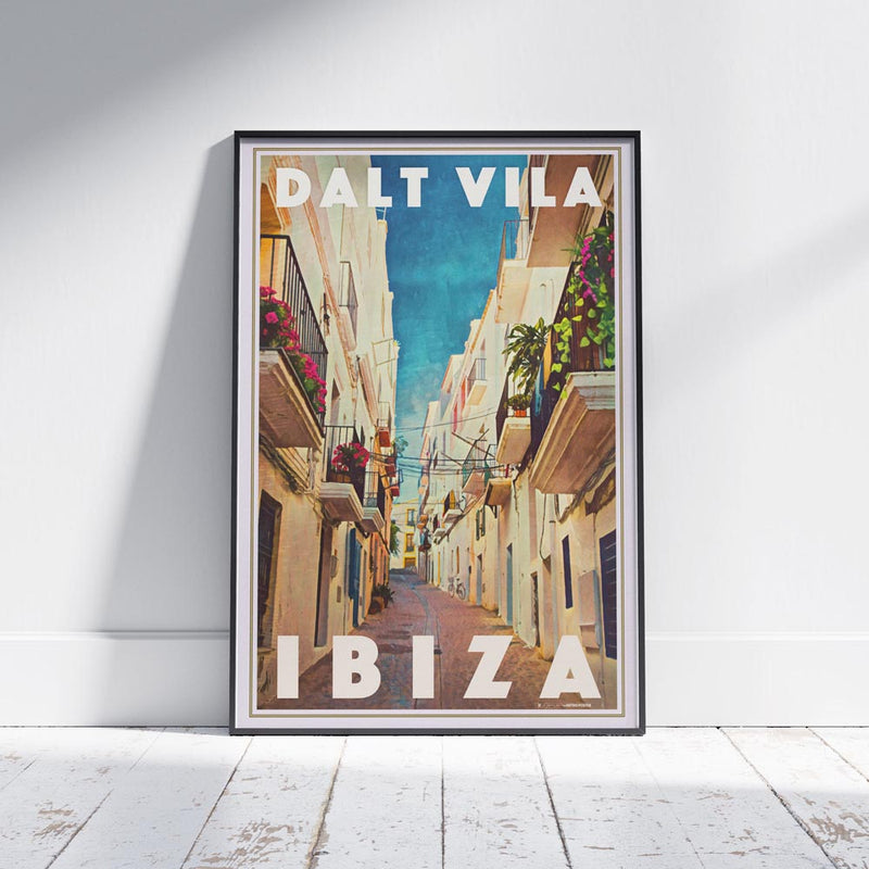 Framed Dalt Vila Ibiza Travel Poster on a white wooden floor, depicting a charming Mediterranean street in Ibiza’s historic old town. Limited edition, 300 copies