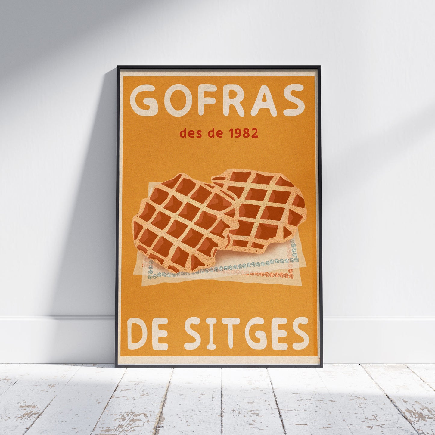 Sitges Waffles Poster by Cha framed on a white wooden floor, showing two golden waffles on patterned napkins over an ochre background. Retro halftone texture visible. Limited edition of 300 prints.