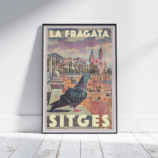 Framed Sitges Pigeon La Fragata travel poster displayed on a wall with the church of Sant Bartomeu i Santa Tecla in the background