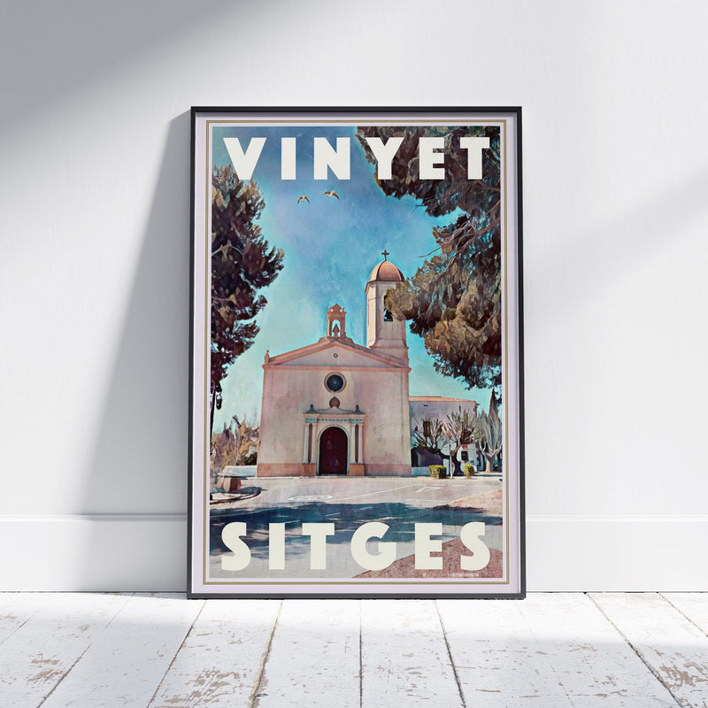 Framed view of Alecse’s Vinyet Sitges poster, depicting the Ermita del Vinyet surrounded by pines and blue sky.
