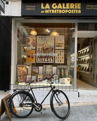 The shop window of La Galerie by Myretroposter in Sitges, showcasing a curated selection of vintage wall art prints and pop-art-inspired posters. The display features iconic Sitges posters, retro comic-style artwork from the Soft Pop Studio™ collection by Cha, and Spanish-themed designs like La Crema Catalana. A mix of bold colors, nostalgic typography, and artistic diversity highlights the gallery’s unique blend of travel and pop culture aesthetics.