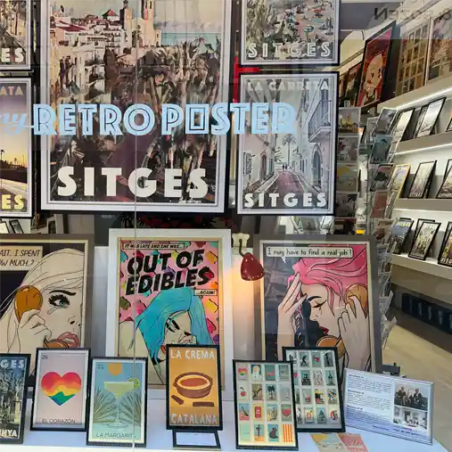 The shop window of La Galerie by Myretroposter in Sitges, showcasing a curated selection of vintage wall art prints and pop-art-inspired posters. The display features iconic Sitges posters, retro comic-style artwork from the Soft Pop Studio™ collection by Cha, and Spanish-themed designs like La Crema Catalana. A mix of bold colors, nostalgic typography, and artistic diversity highlights the gallery’s unique blend of travel and pop culture aesthetics.