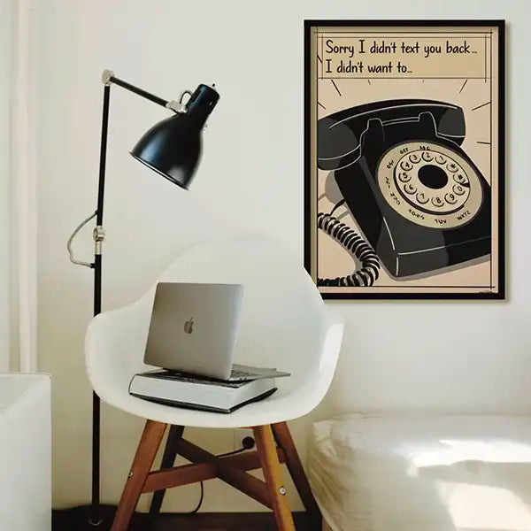 Framed retro poster with vintage rotary phone and humorous quote above a modern chair with laptop, minimalist home office wall decor