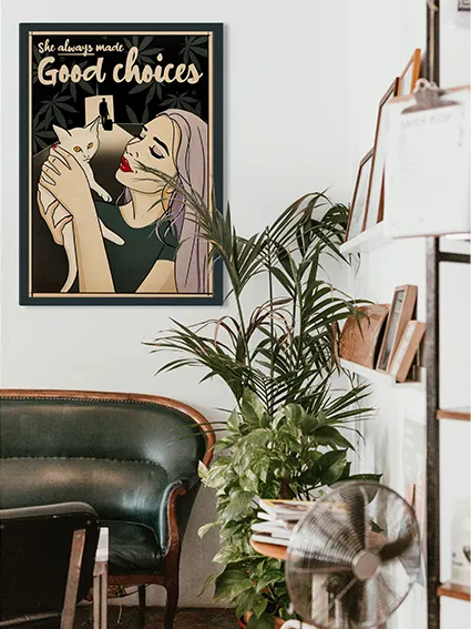 A framed pop art-style poster by Cha for Soft Pop Studio hangs on a white wall. It features a woman with long lilac hair, red lips, and gold hoop earrings, lovingly holding a white cat. The phrase “She always made Good choices” is written at the top. A shadowy silhouette of a man with a suitcase appears in the background, hinting at a past decision. The setting includes a vintage green leather couch, plants, and a bookshelf, creating a cozy atmosphere.