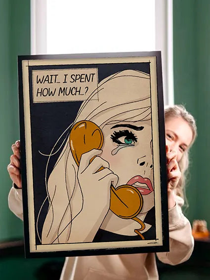 A woman holds up a framed pop art-style poster featuring a close-up of a blonde woman with blue eyes and a tear rolling down her cheek. She is holding a vintage orange telephone to her ear with a distressed expression. The poster has a beige background with black outlines and a comic book-style speech bubble that reads, “WAIT… I SPENT HOW MUCH..?” The edges of the poster have a slightly worn, retro aesthetic. The person holding the frame is partially visible, smiling behind it, wearing a light-colored sweat