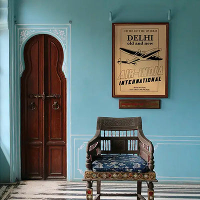Vintage-style Delhi travel poster displayed in an elegant Indian-inspired interior with turquoise walls, carved wooden door, antique chair and framed Air India artwork above. Limited edition wall art from The Great Indian Decor™ collection by Shree