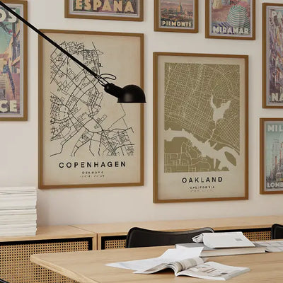 Modern workspace with a gallery wall featuring minimalist city map posters from the Wanderer Maps™ collection by Cha, highlighting Copenhagen and Oakland alongside vintage travel prints.